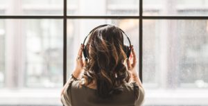 woman with headphone facing a window with her back to viewer