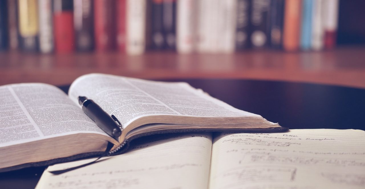 open book with a black fountain pen on top of it and a library bookshelf in the background