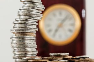 stack of coins in the foreground with a clock in the background