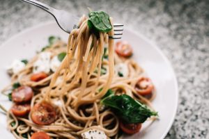 Spaghetti on a fork with the plate in the background, with tomatoes , basil and cheese.
