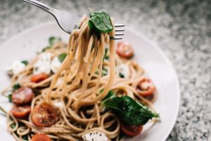 Spaghetti  on a fork with the plate in the background, with tomatoes , basil and cheese.