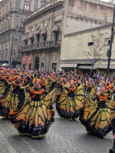 Dancers dressed in butterfly-themed traditional dresses performing in a parade on a city street.