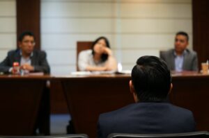 Back view of a person addressing a group of people at a table in a meeting room