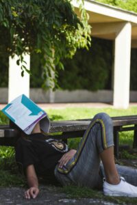 A person lying on a bench outdoors with a book covering their face.