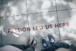 A sidewalk with the phrase 'PASSION LED US HERE' etched into it, with two pairs of shoes standing side by side, symbolizing teamwork and shared purpose.