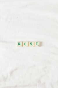 Scrabble tiles spelling "REST" on a white bedsheet, emphasizing the importance of self-care and slowing down