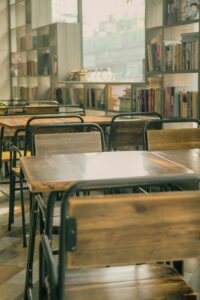 A well-lit library café with wooden tables and chairs, surrounded by bookshelves filled with a diverse collection of books