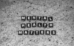 Black and white image with the words "MENTAL HEALTH MATTERS" spelled out using small black tiles with white letters, arranged on a speckled countertop