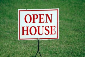 Open house sign with red lettering displayed on a grassy lawn.